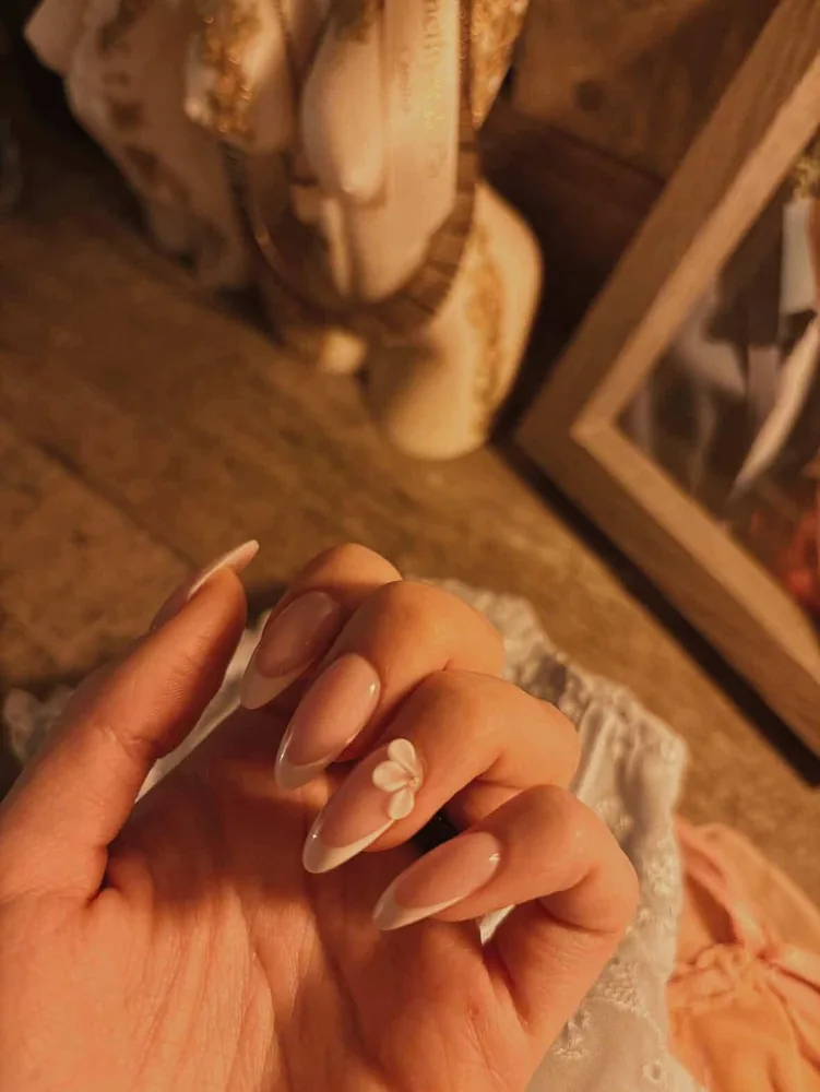 Almond nails in a soft cream French finish with a single sculpted white flower accent