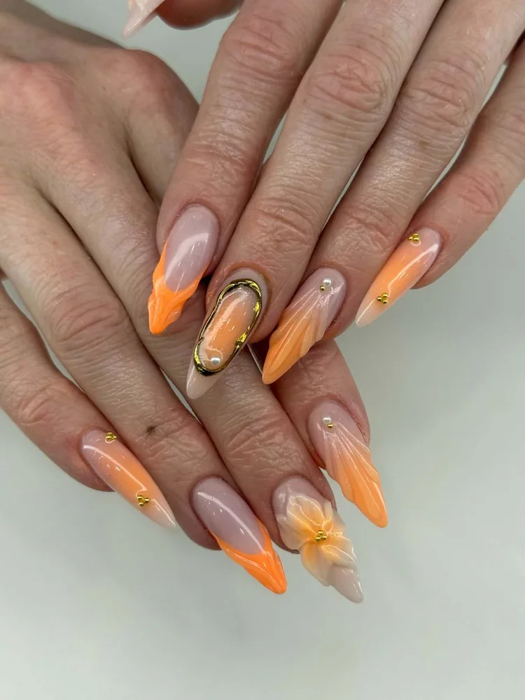 Long almond nails in a peach and orange ombré with a sculpted 3D flower, gold wire framing and pearl accents
