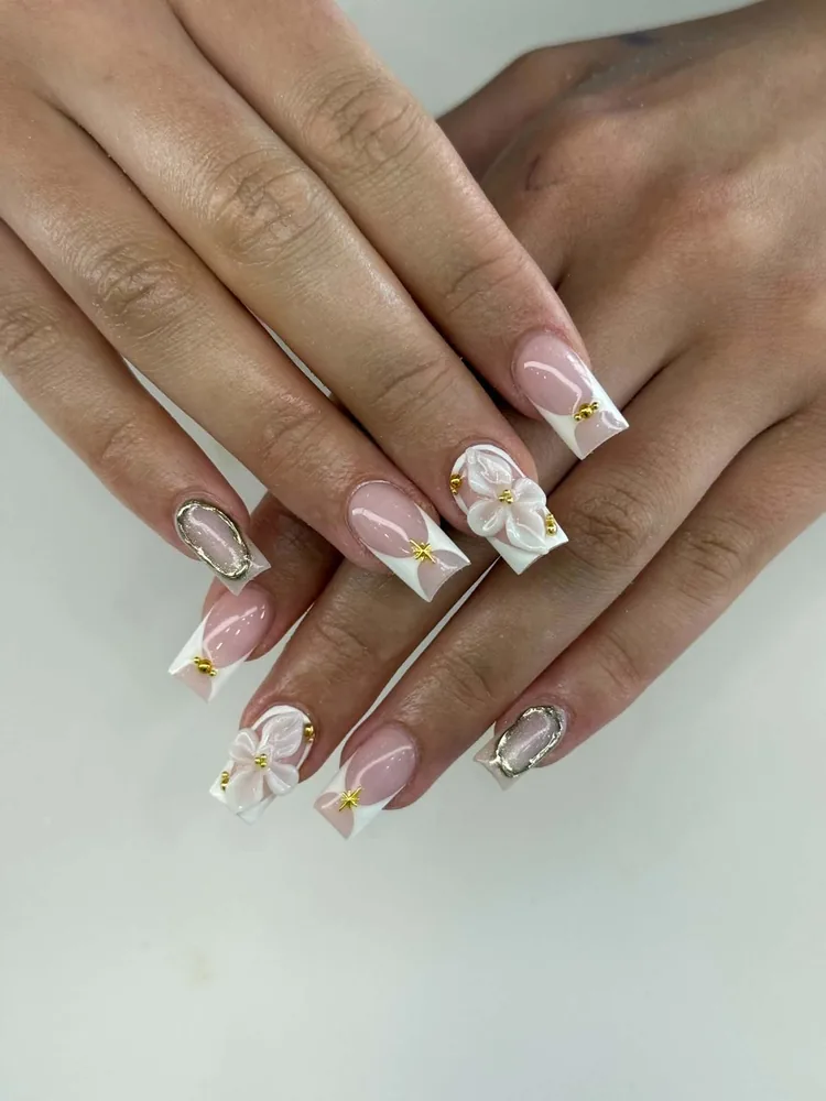 Square nails with white French tips, sculpted 3D white flowers, gold beads and gold starburst accents
