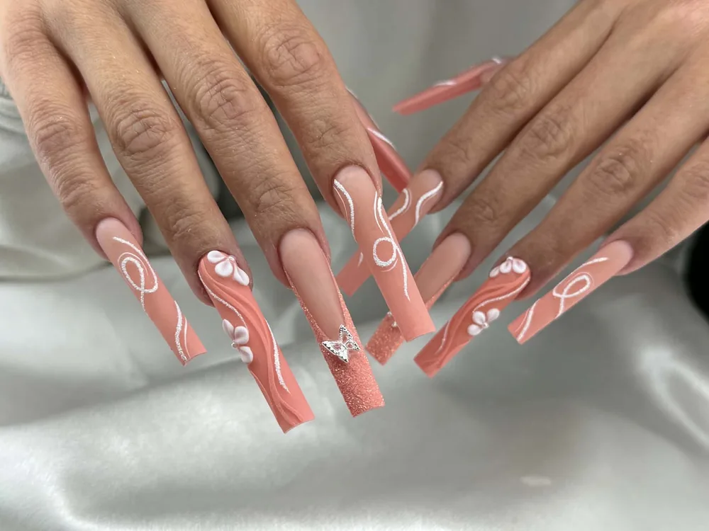 Long square nails in coral with white swirl line work, sculpted white flowers, glitter and a silver butterfly charm