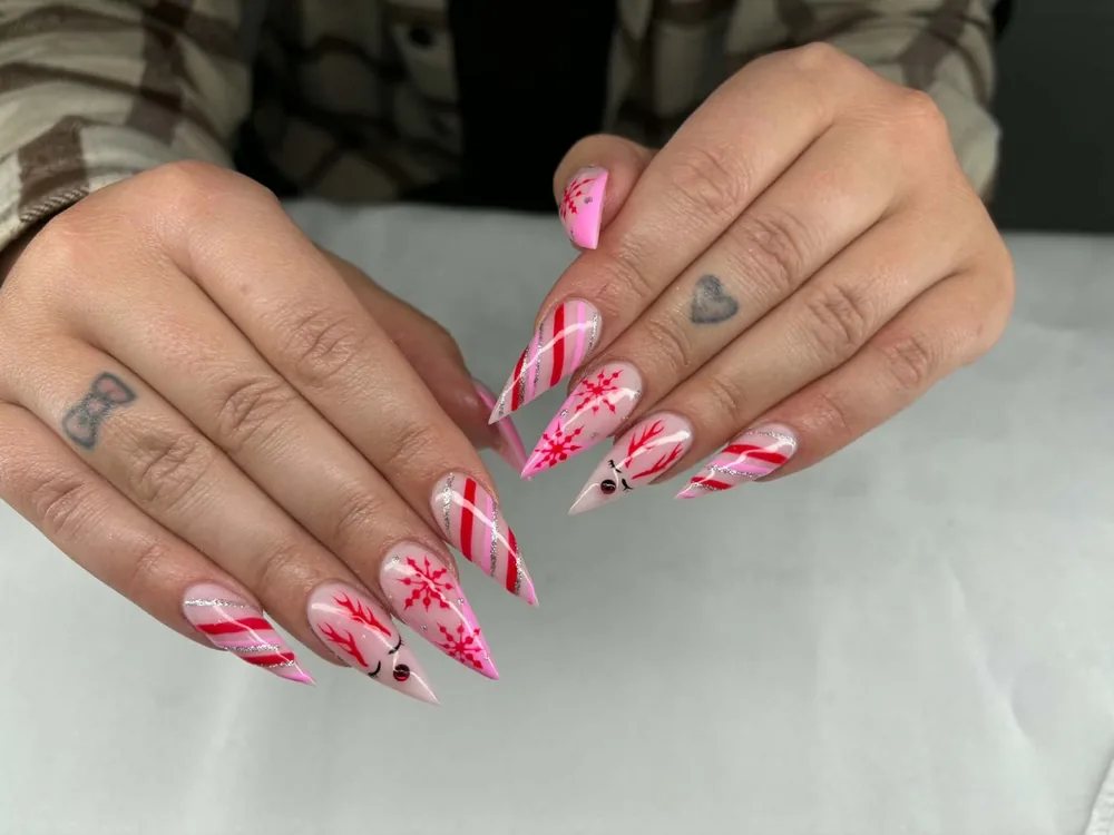 Stiletto Christmas nails with candy-cane stripes, red snowflakes and hand-painted reindeer faces on a pink base